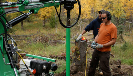 Two installers installing a pier right next to a tree stump.