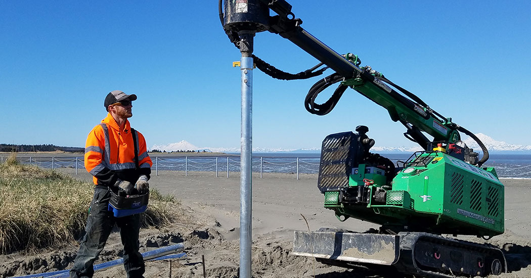 Installing metal posts along an Alaskan beach with volcanoes in the background.